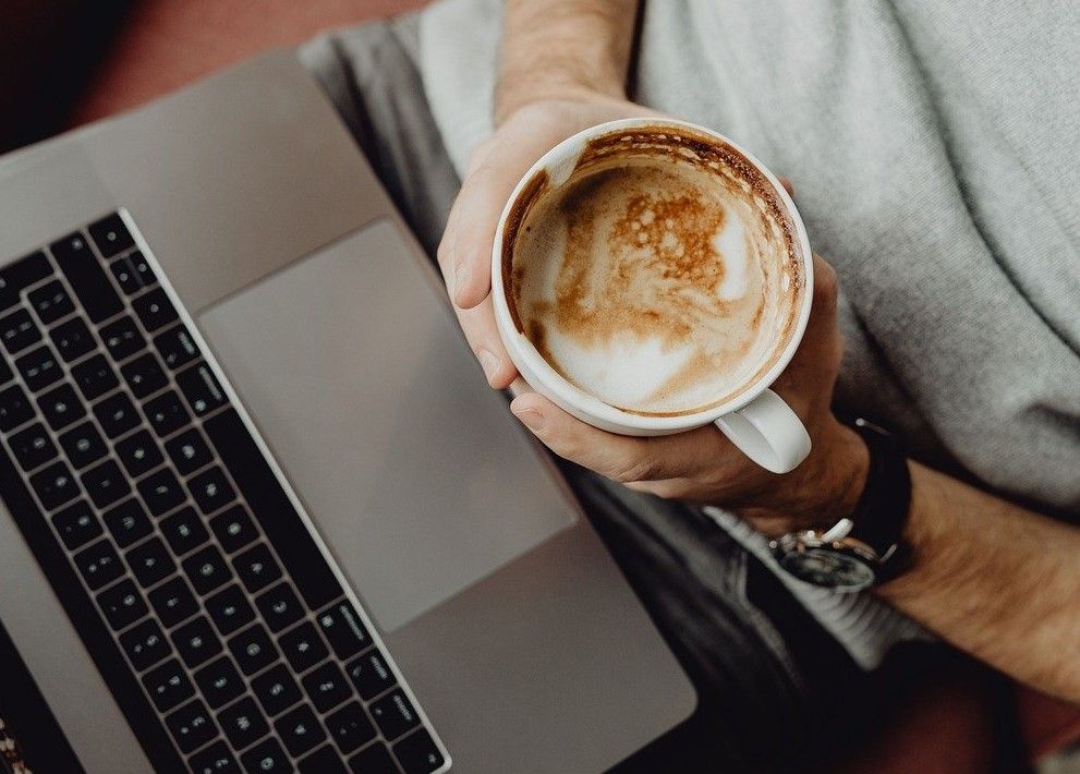 Person sitter vid laptop med kaffekopp i handen