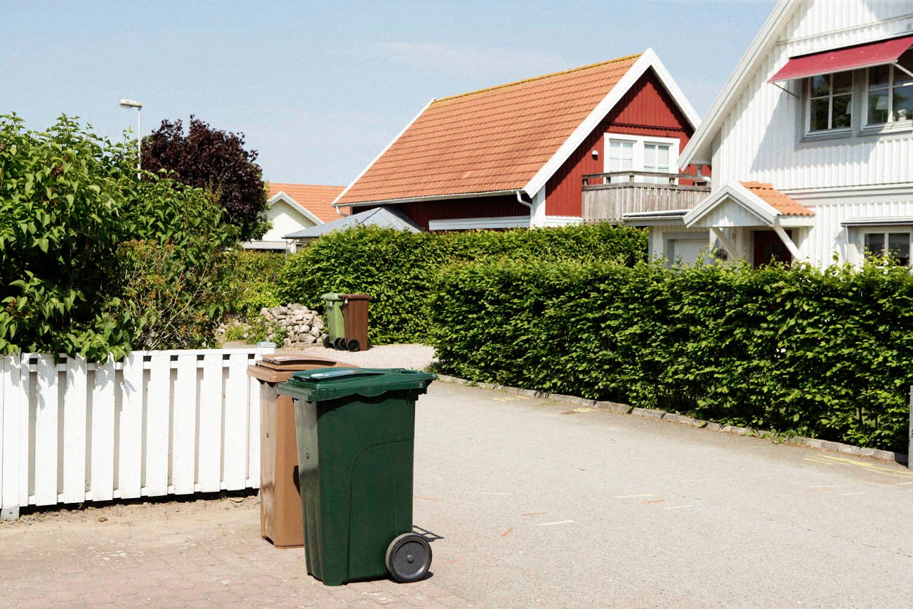 Ett grönt och ett brunt sopkärl ställda vid tomtgräns