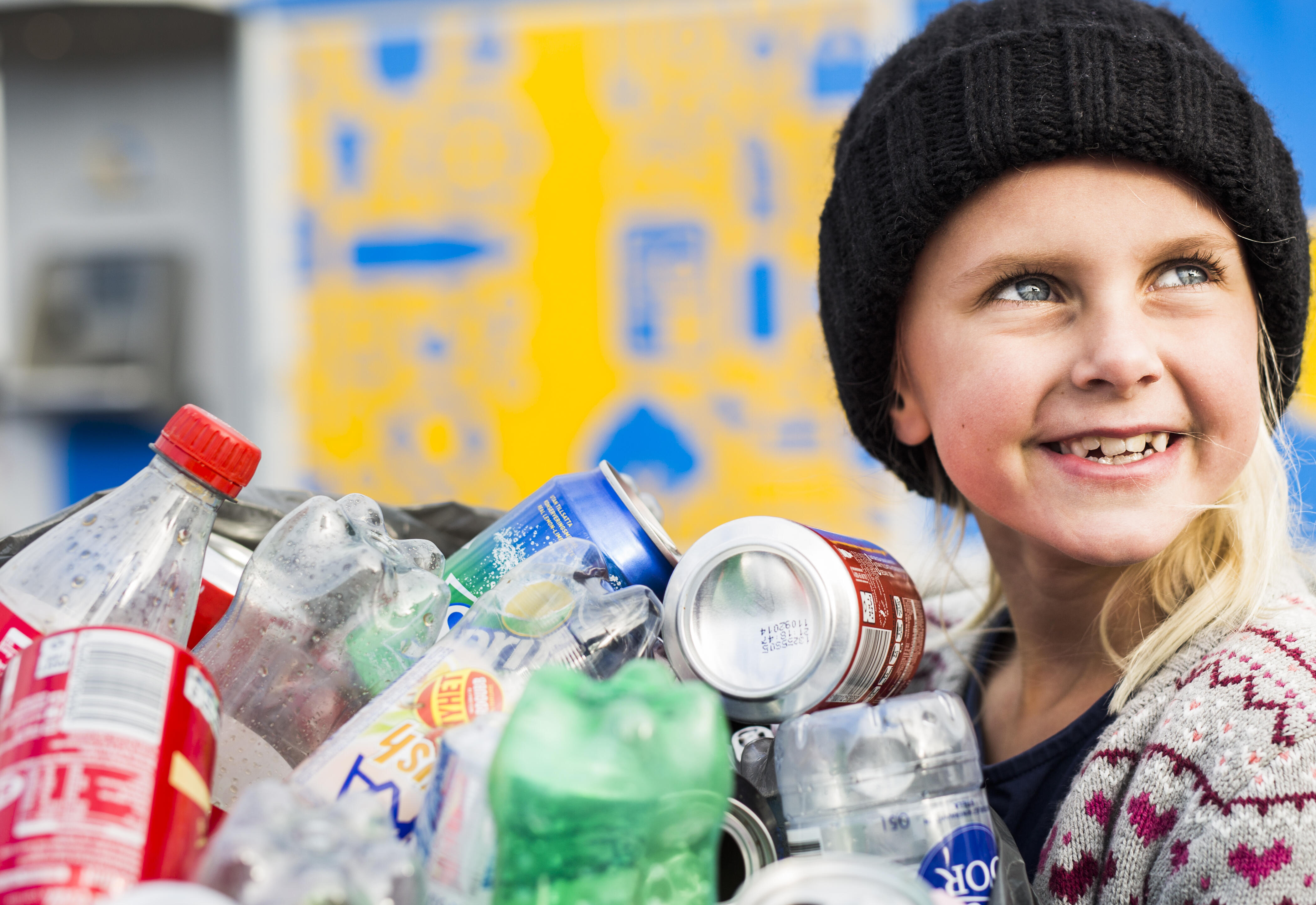 En flicka håller i en säck med pant och tittar leende 