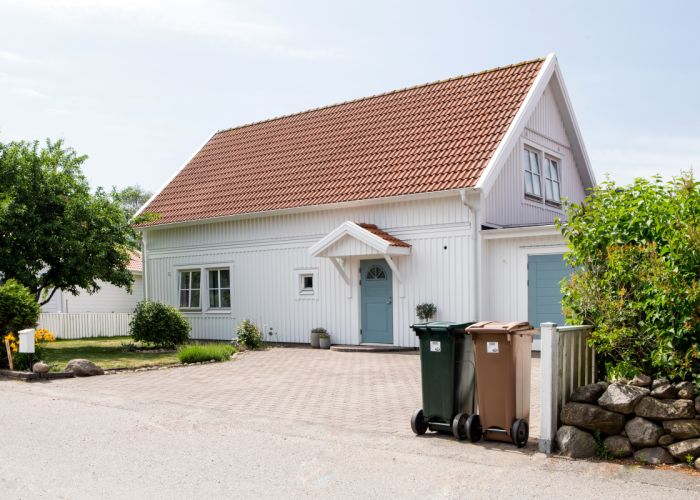 Två kärl placerade vid tomtgräns med handtag och hjul mot gata