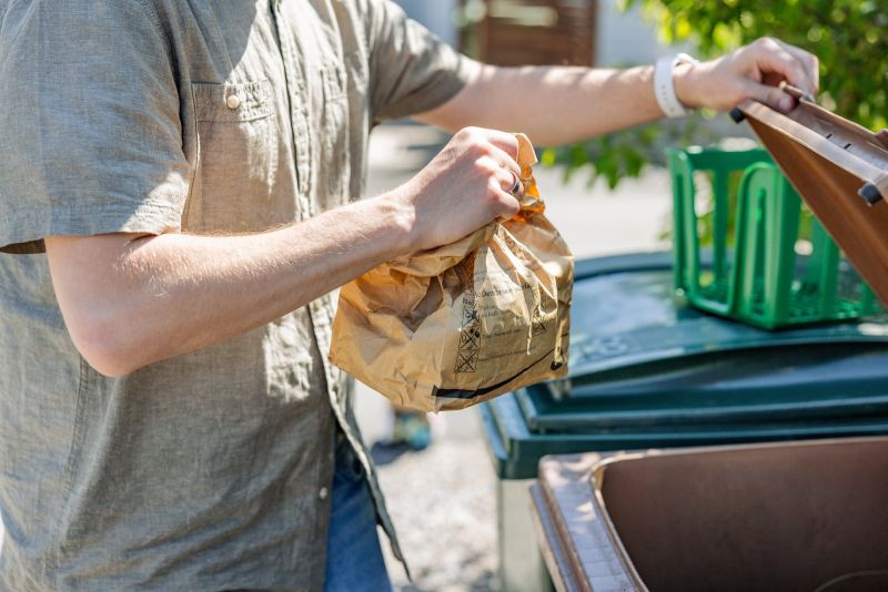 En person slänger en matavfallspåse i ett brunt avfallskärl