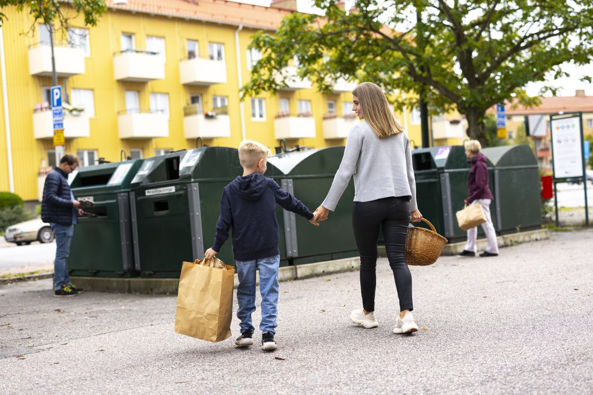 En mamma och ett barn går med påsar i händerna till en återvinningsstation