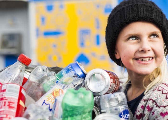 En flicka håller i en säck med pant och tittar leende 