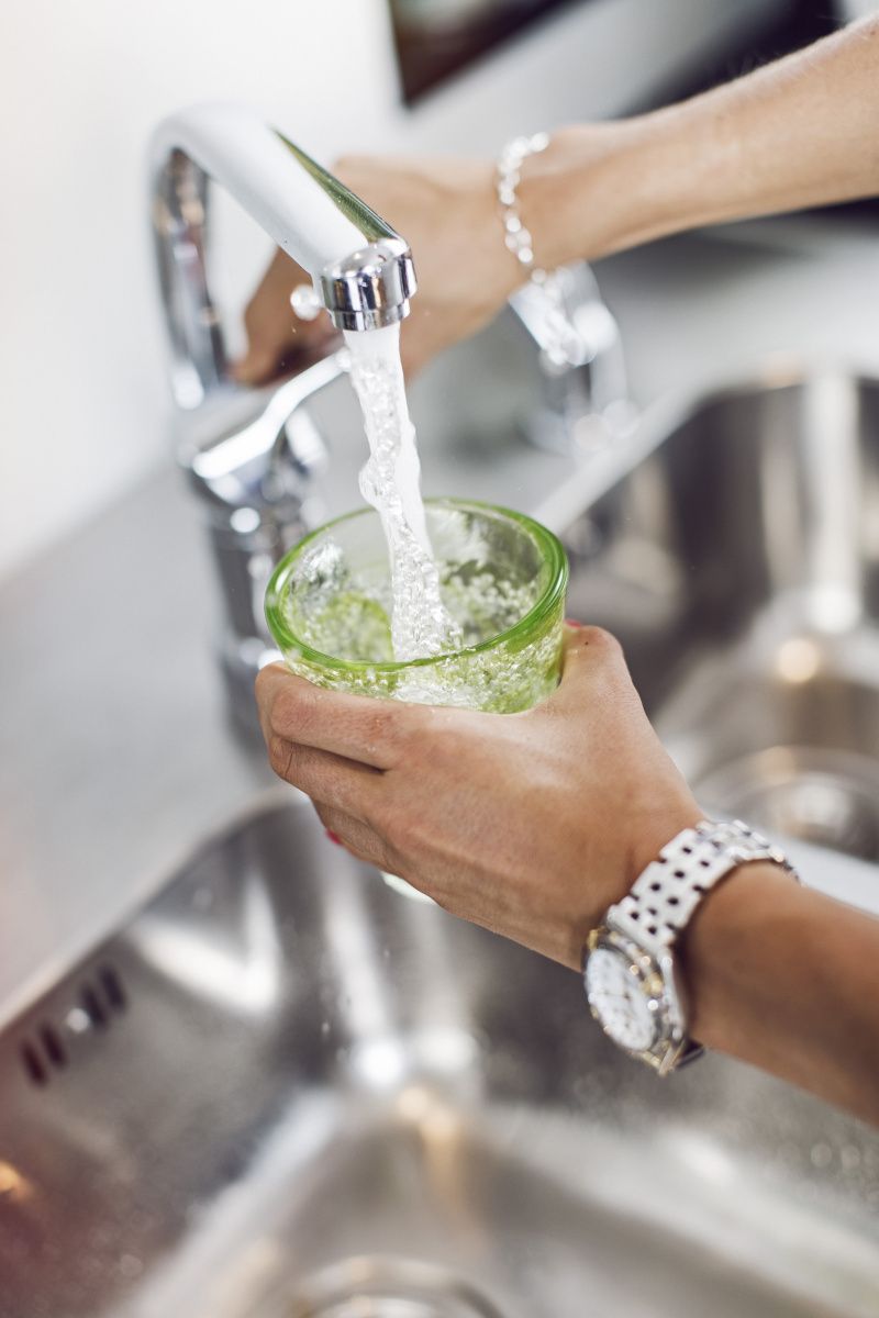 Hand håller grönt glas som fylls med vatten under en kran. 