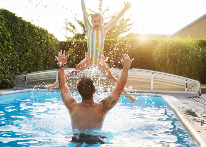 En man står i en pool och kastar upp ett barn i luften