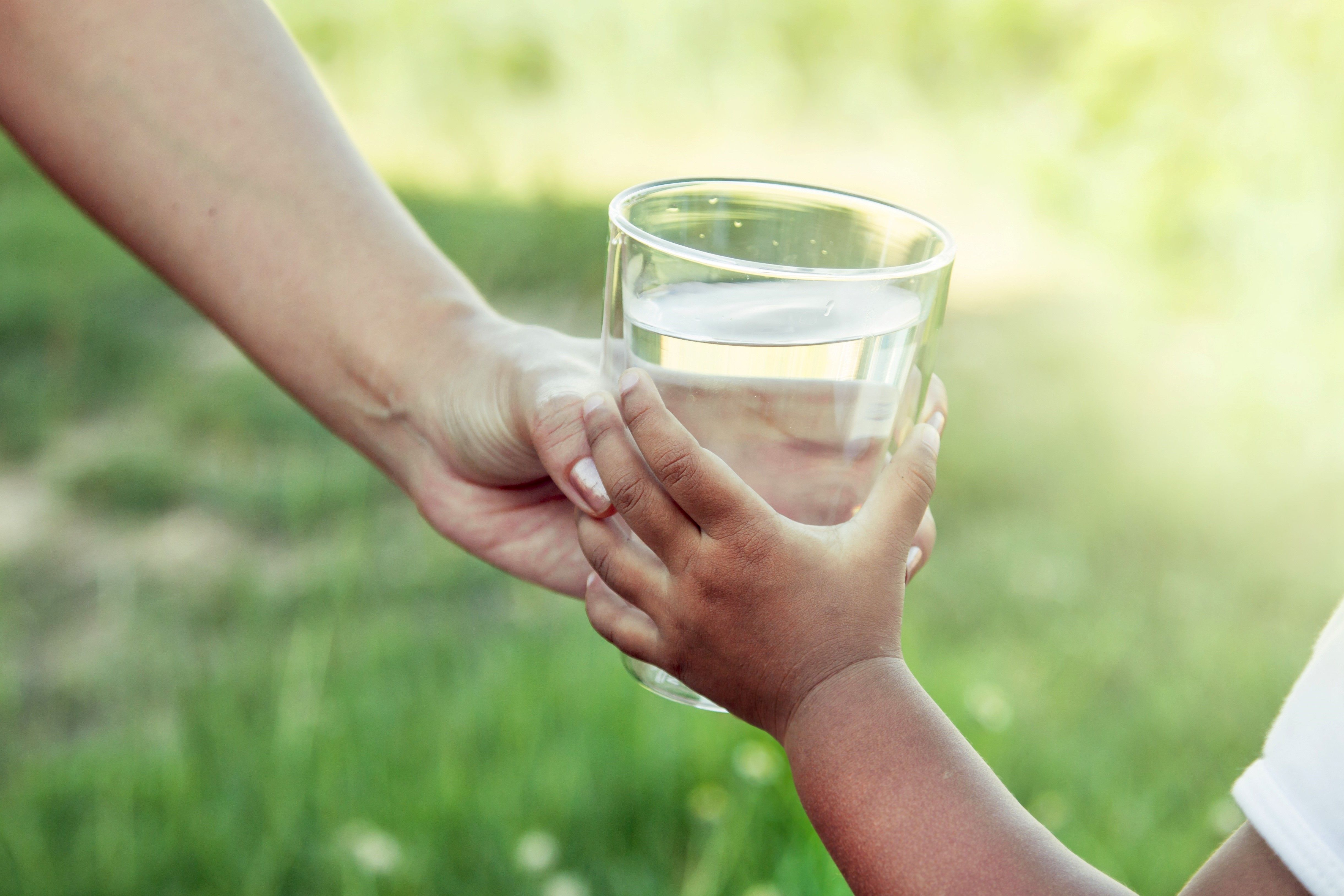 En vuxenhand sträcker över ett vatten glas till en barnhand